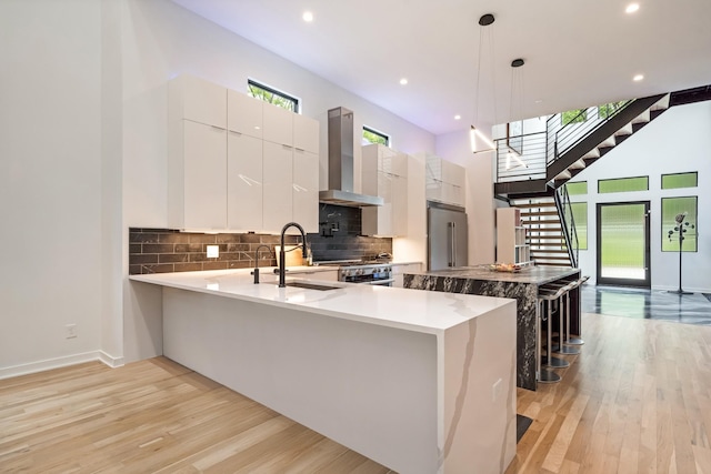 kitchen featuring wall chimney range hood, modern cabinets, light wood-style flooring, decorative backsplash, and baseboards