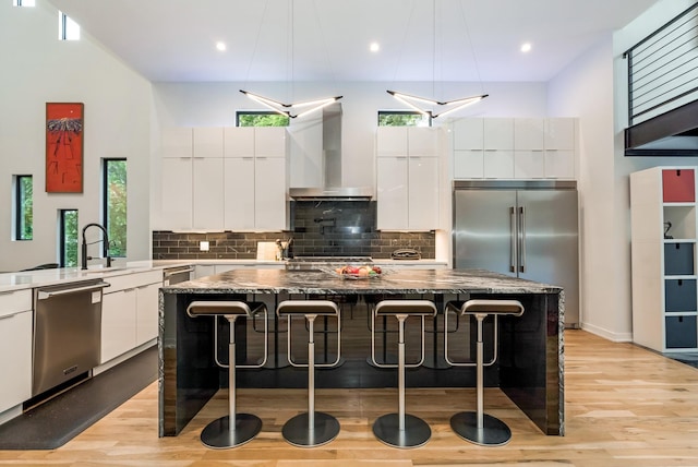 kitchen with appliances with stainless steel finishes, wall chimney exhaust hood, modern cabinets, recessed lighting, and a high ceiling