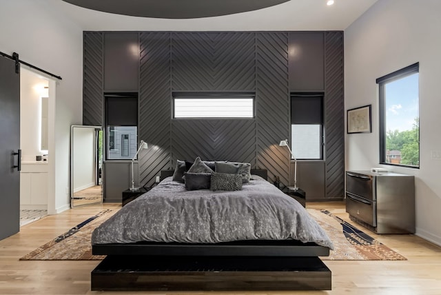 bedroom with a barn door, an accent wall, light wood-type flooring, baseboards, and recessed lighting