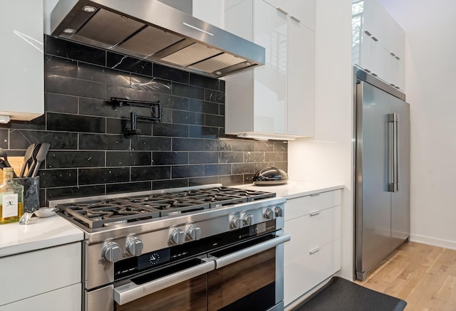 kitchen featuring high end appliances, wall chimney exhaust hood, and modern cabinets