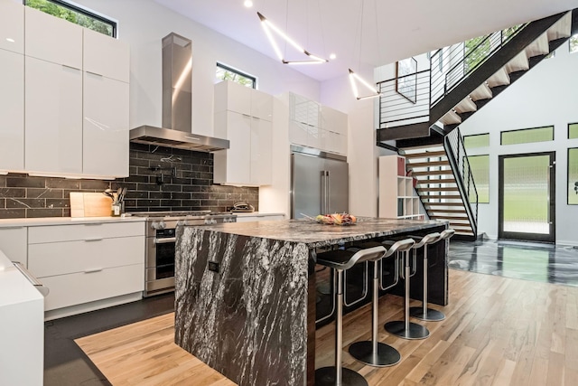 kitchen with wall chimney exhaust hood, premium appliances, modern cabinets, a breakfast bar area, and a high ceiling