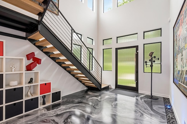 entrance foyer featuring stairs, a towering ceiling, and baseboards