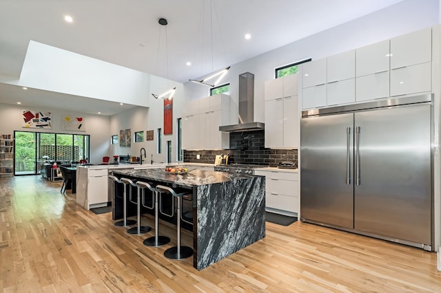 kitchen with built in refrigerator, wall chimney exhaust hood, modern cabinets, a peninsula, and light wood finished floors