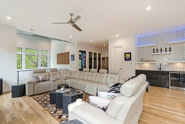living room featuring wine cooler, wet bar, light wood-type flooring, a ceiling fan, and recessed lighting