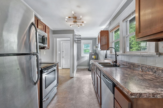 kitchen featuring appliances with stainless steel finishes, dark countertops, a sink, brown cabinetry, and a chandelier