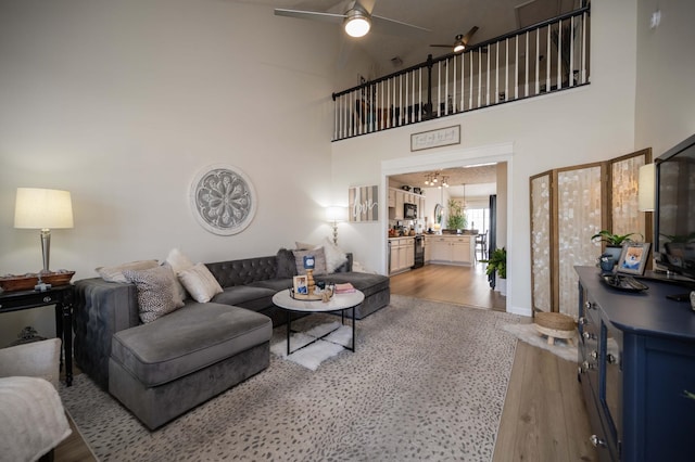 living room featuring wood finished floors, a ceiling fan, and a towering ceiling