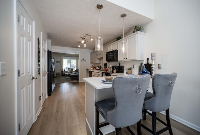 kitchen featuring black appliances, a kitchen bar, light countertops, a peninsula, and light wood-type flooring