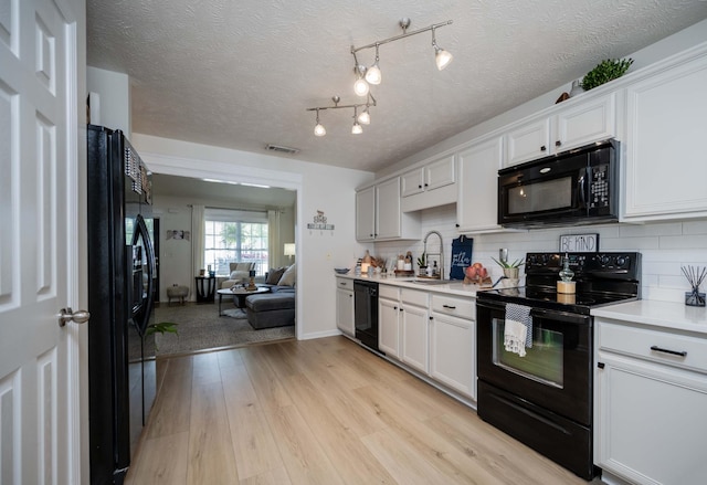 kitchen with black appliances, light countertops, a sink, light wood finished floors, and backsplash