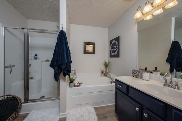 full bathroom with wood finished floors, a shower stall, a garden tub, vanity, and a textured ceiling