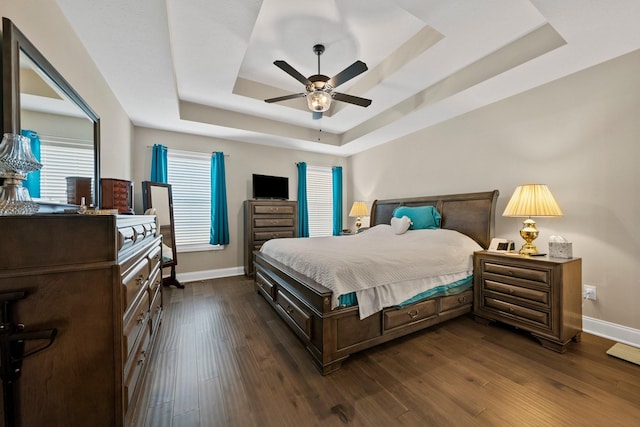 bedroom featuring a tray ceiling, baseboards, dark wood-style flooring, and a ceiling fan
