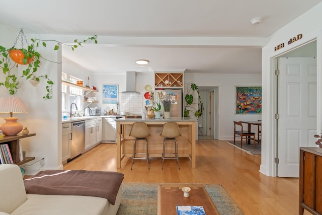 kitchen with stainless steel appliances, wall chimney exhaust hood, a kitchen breakfast bar, light countertops, and a kitchen island
