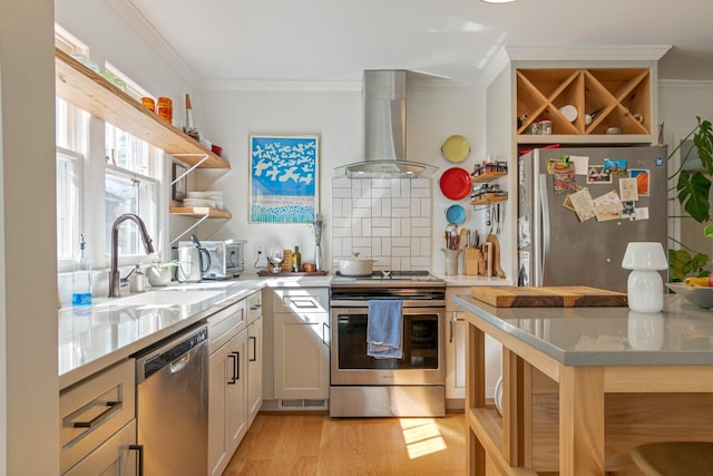 kitchen featuring appliances with stainless steel finishes, wall chimney exhaust hood, light countertops, a sink, and ornamental molding