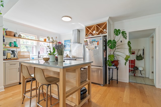kitchen featuring freestanding refrigerator, open shelves, wall chimney exhaust hood, ornamental molding, and light wood finished floors