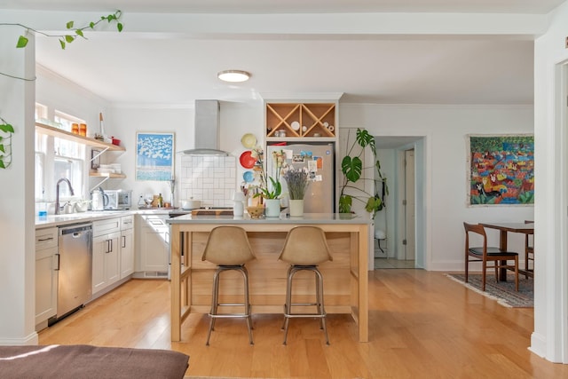 kitchen with wall chimney exhaust hood, appliances with stainless steel finishes, ornamental molding, a sink, and open shelves