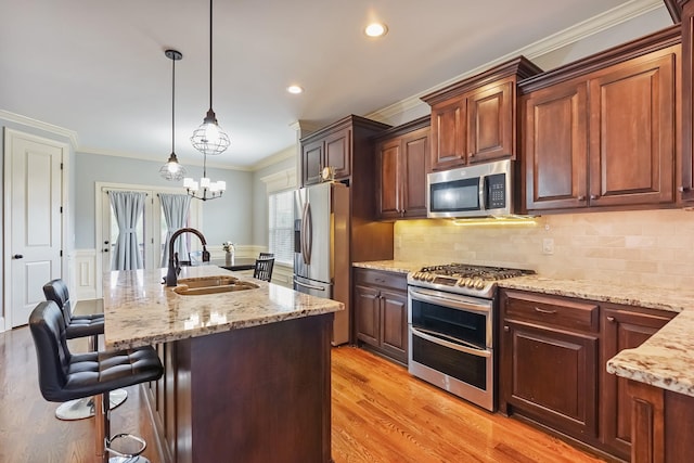 kitchen with appliances with stainless steel finishes, a sink, crown molding, a breakfast bar, and light stone countertops