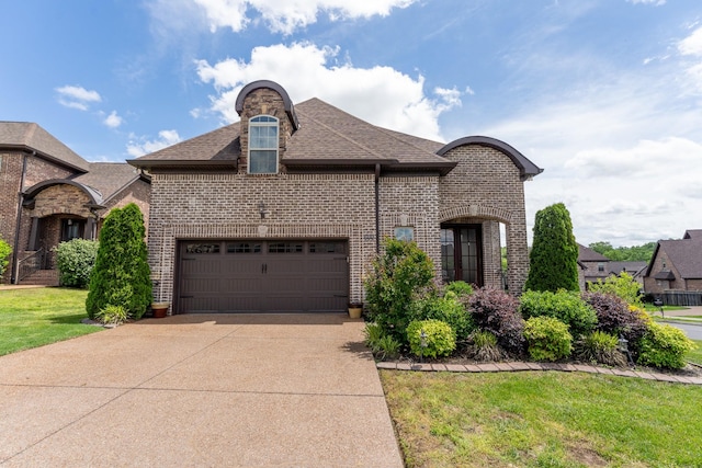 french provincial home with brick siding, an attached garage, roof with shingles, and driveway