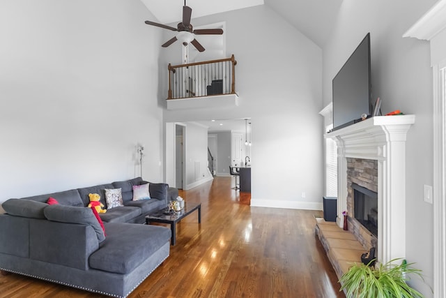 living area with a ceiling fan, a fireplace, wood finished floors, high vaulted ceiling, and baseboards