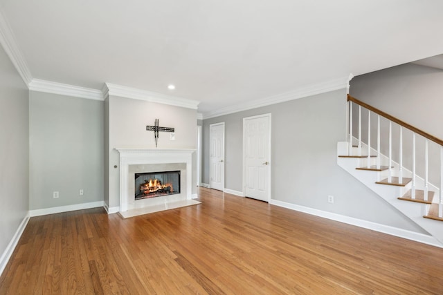 unfurnished living room with crown molding, wood finished floors, stairs, a fireplace with flush hearth, and baseboards