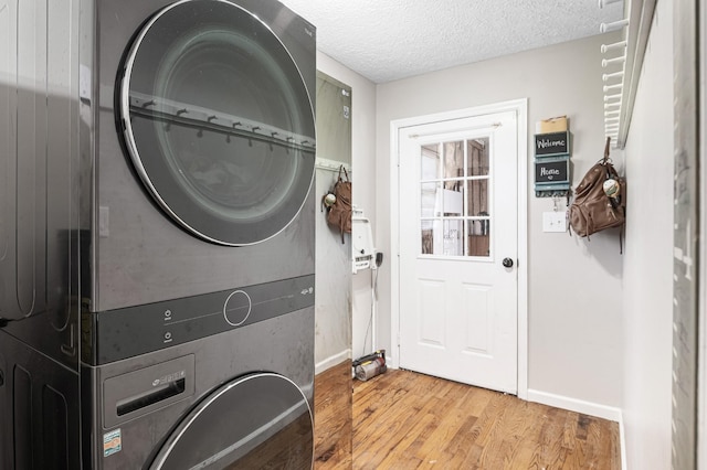 washroom featuring stacked washer / dryer, light wood-type flooring, a textured ceiling, and baseboards