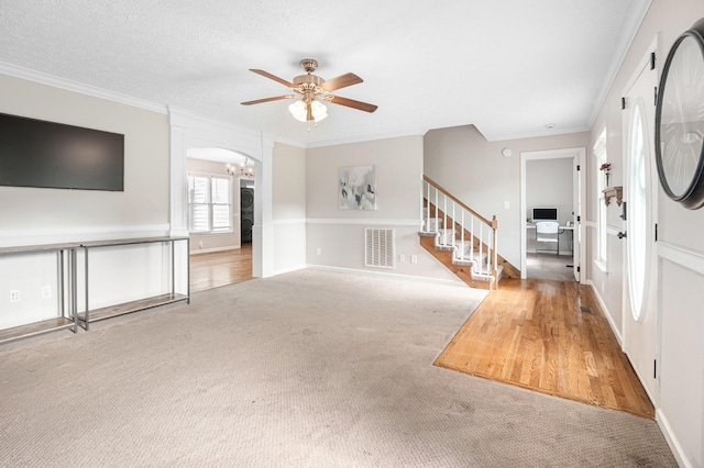 unfurnished living room with stairs, ceiling fan, carpet, crown molding, and arched walkways
