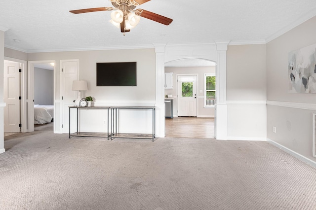 unfurnished living room featuring a ceiling fan, ornamental molding, carpet, baseboards, and arched walkways