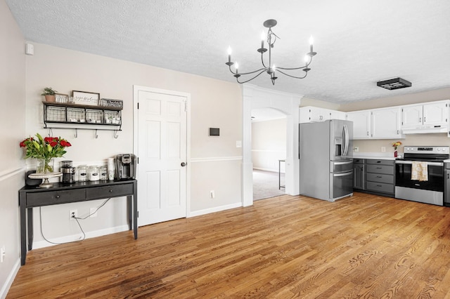 kitchen with appliances with stainless steel finishes, under cabinet range hood, arched walkways, light wood-style floors, and a textured ceiling