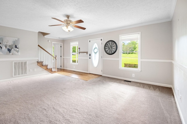 carpeted foyer featuring stairway, a ceiling fan, baseboards, ornamental molding, and a textured ceiling