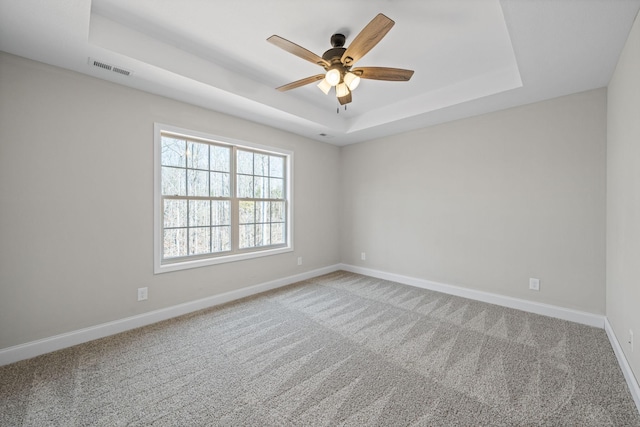 carpeted empty room featuring a raised ceiling, baseboards, and ceiling fan