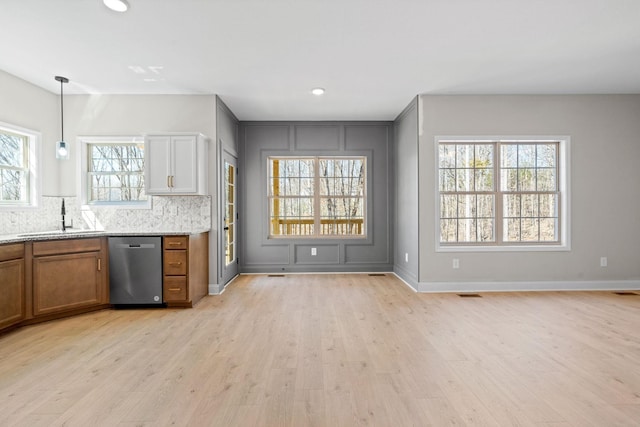 kitchen with a sink, stainless steel dishwasher, brown cabinets, light wood-style flooring, and decorative backsplash