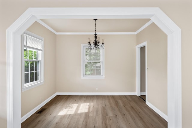 unfurnished dining area featuring wood finished floors, a chandelier, ornamental molding, and baseboards