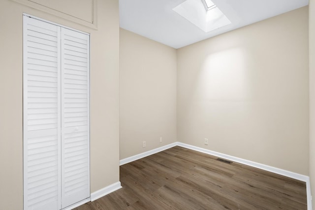 unfurnished bedroom featuring a skylight, dark wood-type flooring, baseboards, and a closet