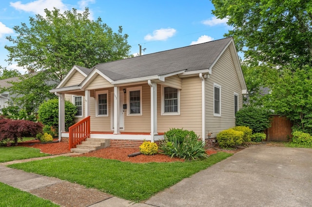bungalow-style home with covered porch, a shingled roof, and a front yard