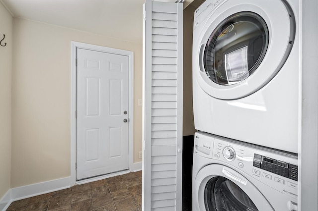 laundry room with stacked washer / drying machine, baseboards, and stone finish flooring