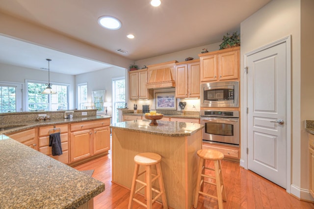 kitchen with appliances with stainless steel finishes, light brown cabinetry, a center island, a breakfast bar area, and recessed lighting