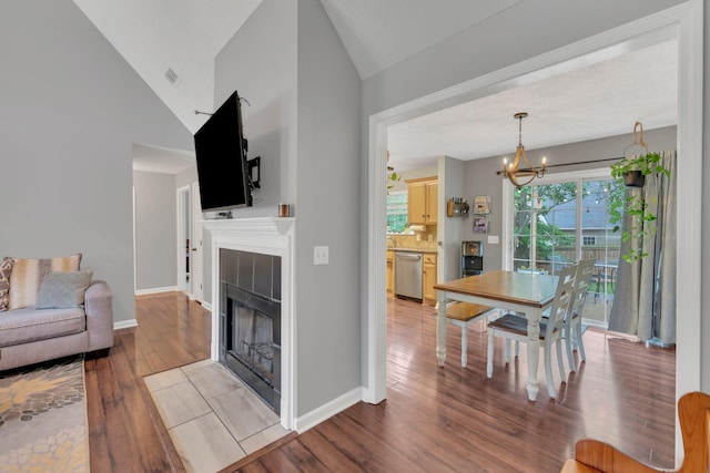 living room with a tiled fireplace, a chandelier, light wood-style floors, baseboards, and vaulted ceiling