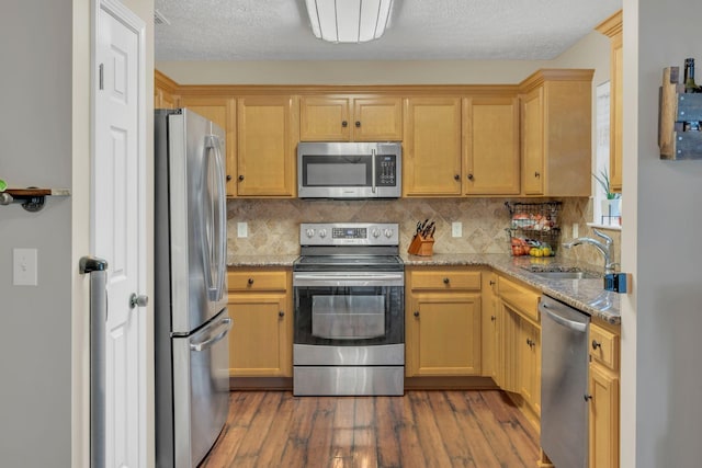 kitchen featuring stainless steel appliances, a sink, wood finished floors, backsplash, and light stone countertops