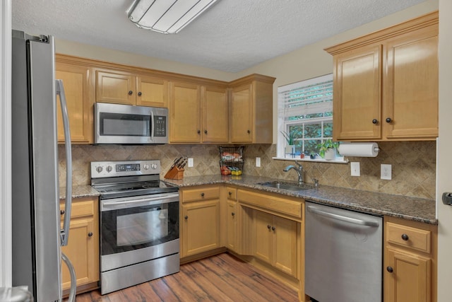 kitchen with appliances with stainless steel finishes, a sink, wood finished floors, tasteful backsplash, and a textured ceiling