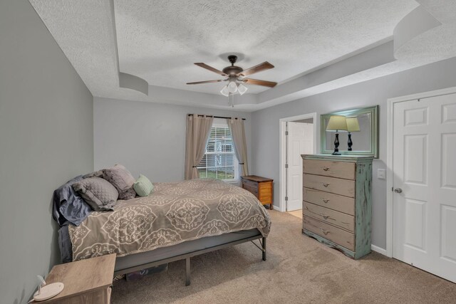 bedroom with a tray ceiling, a textured ceiling, light carpet, a ceiling fan, and baseboards