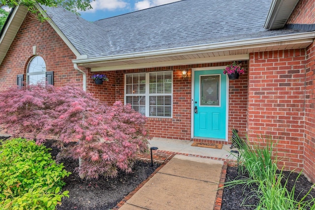 entrance to property featuring a shingled roof and brick siding