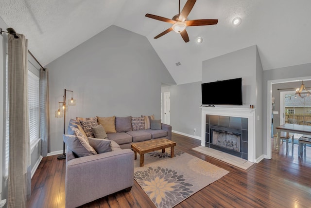 living area with a ceiling fan, a tiled fireplace, high vaulted ceiling, wood finished floors, and baseboards