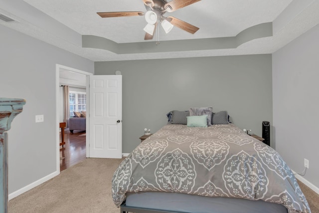 carpeted bedroom with a tray ceiling, baseboards, and a ceiling fan