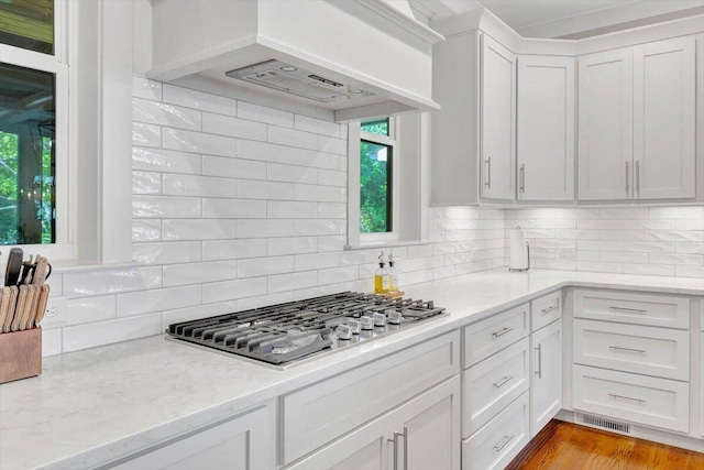 kitchen with stainless steel gas stovetop, tasteful backsplash, white cabinets, and premium range hood