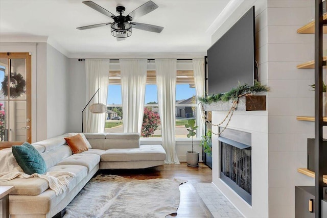 living room featuring a fireplace, wood finished floors, ornamental molding, and a ceiling fan
