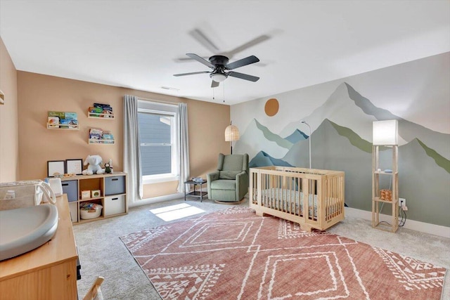 carpeted bedroom featuring a crib, ceiling fan, and baseboards