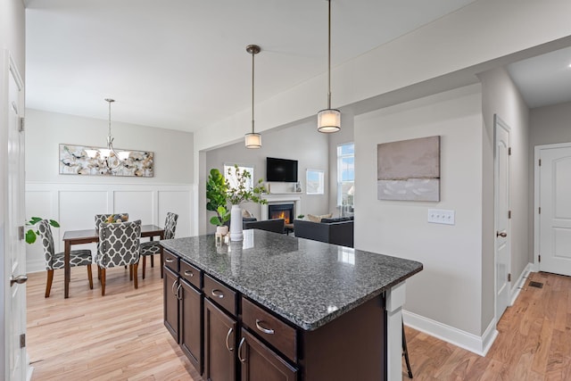5902 Covent Ln, Smyrna, TN 37167 - kitchen with dark brown cabinets, light wood finished floors, a lit fireplace, decorative light fixtures, and a wainscoted wall