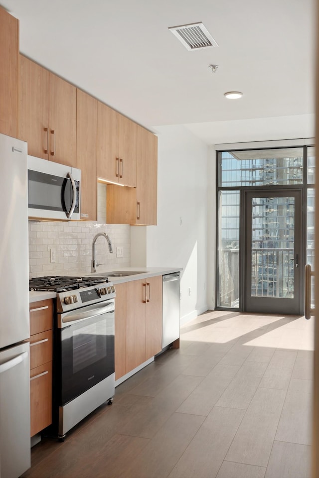 kitchen with appliances with stainless steel finishes, tasteful backsplash, light brown cabinets, light countertops, and baseboards