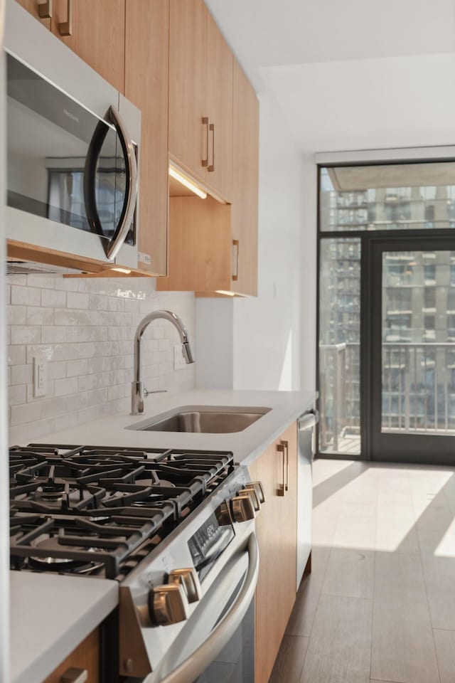kitchen featuring appliances with stainless steel finishes, a sink, backsplash, light countertops, and light brown cabinets