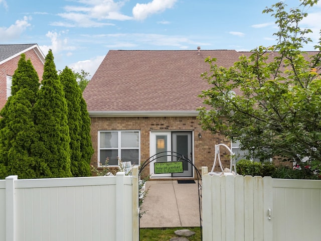 view of front of house featuring a shingled roof, fence, brick siding, and a gate