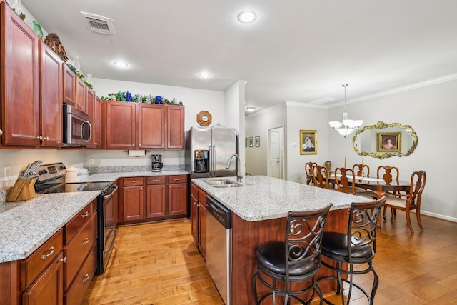 kitchen featuring stainless steel appliances, a sink, light wood-style flooring, crown molding, and a kitchen breakfast bar