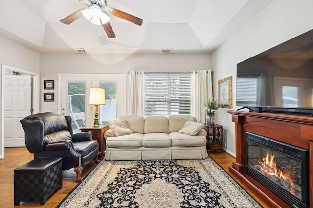 living area featuring ceiling fan, wood finished floors, lofted ceiling, healthy amount of natural light, and a tray ceiling